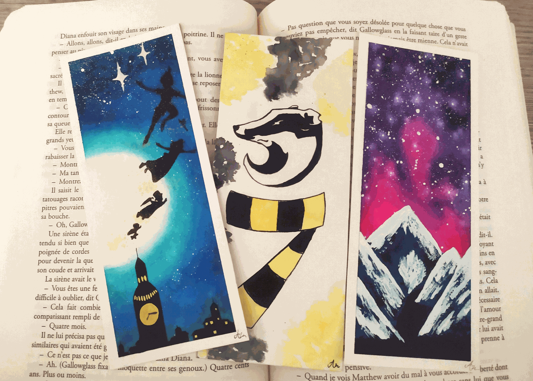 3 marque-pages en aquarelle colorés sur un fond d'une page de livre